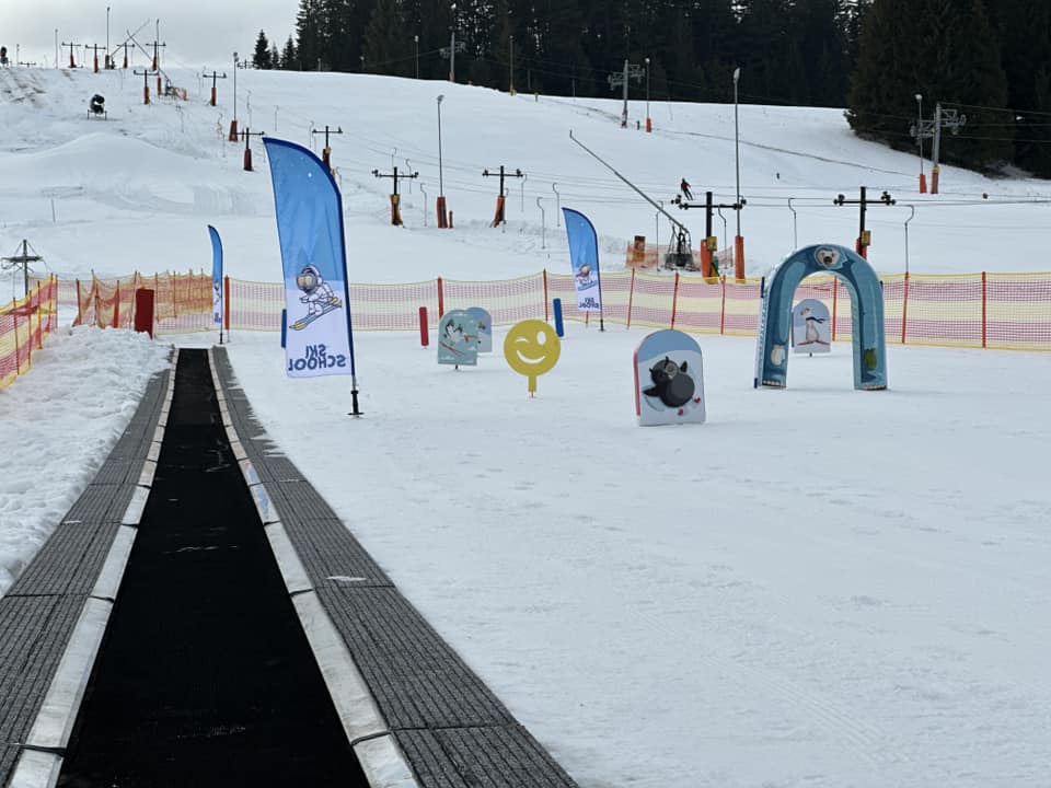 Detský park s pojazdným kobercom, vlajkami Ski School a farebnými prekážkami